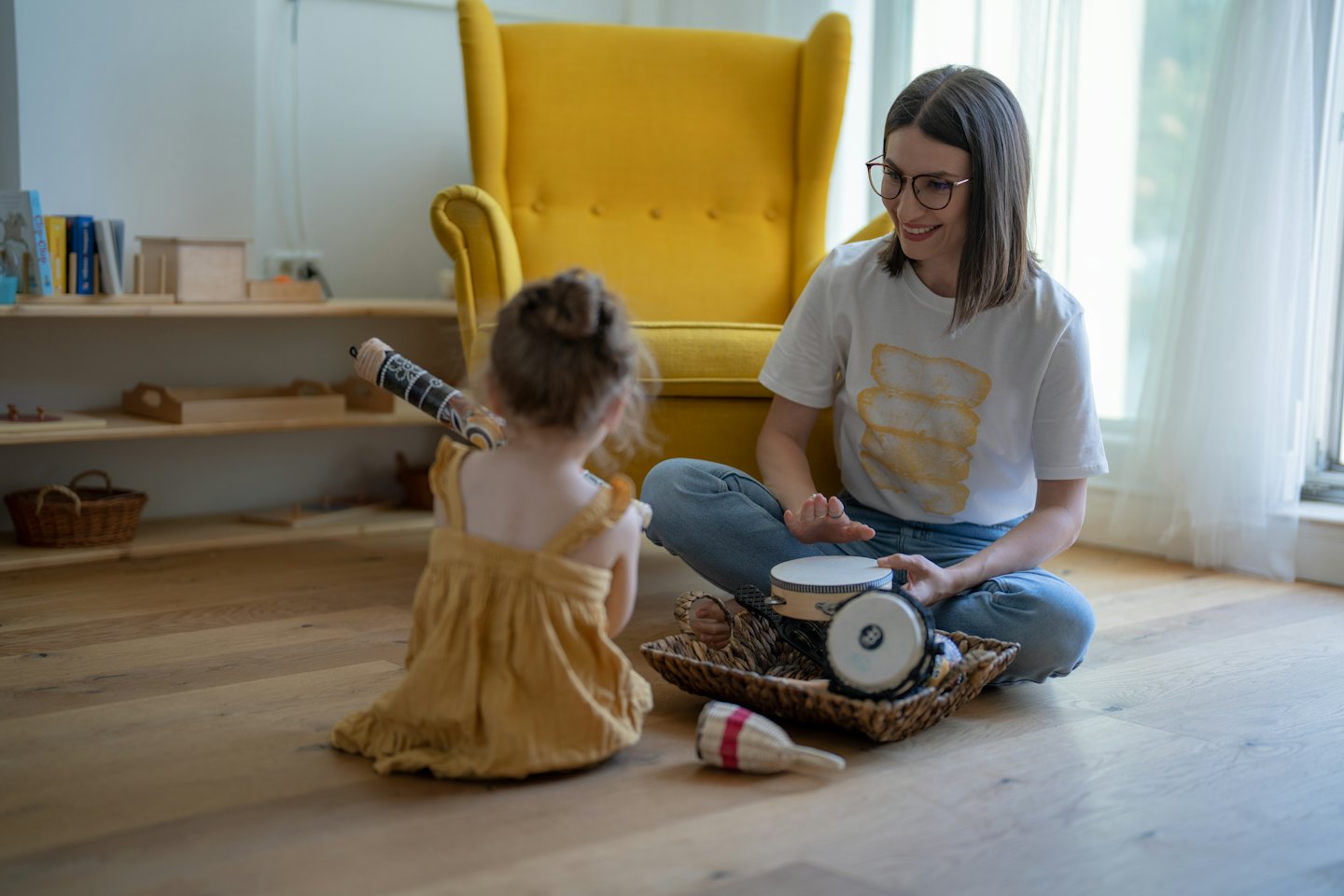 Volwassene speelt handtrommel terwijl kind een stokinstrument vasthoudt.